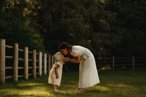 A mum is kissing her daughter on the grass with fence at back