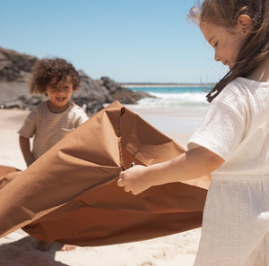 a boy and a girl are holding each corner of the picnic blanket and setting it up on the beach.