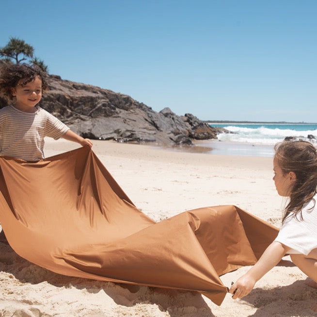 two kids are setting up the picnic blanket on the beach.