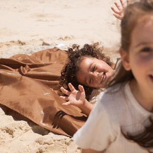 a boy and a girl are playing on the picnic blanket on the beach.
