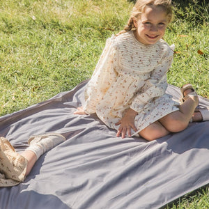 A kid is sitting on the picnic blanket in the park and smiling.
