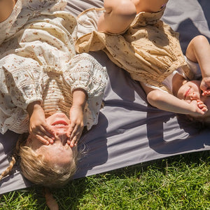 two kids are laying on the picnic blanket, and blocking their eyes with their hands.